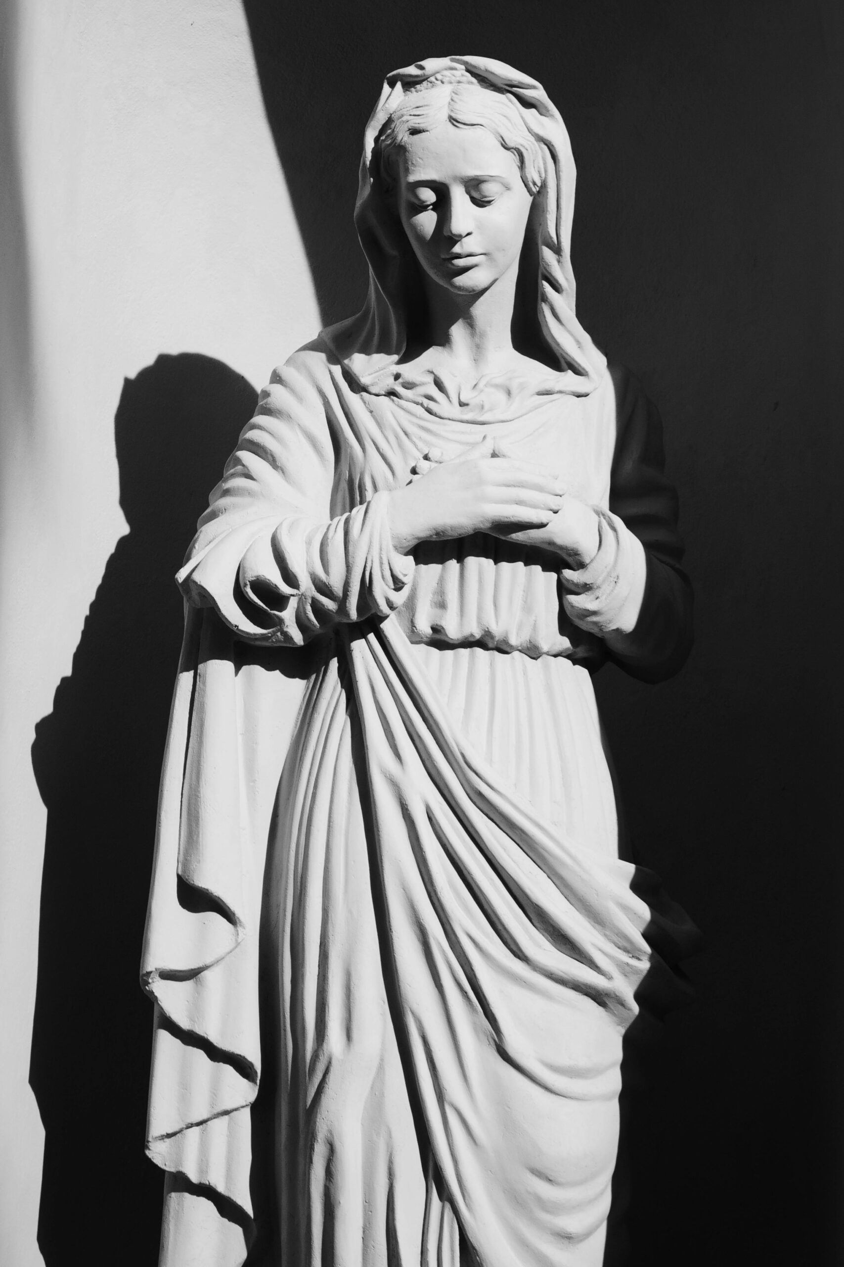 Black and white photograph of Virgin Mary sculpture casting a subtle shadow, evoking a sense of serenity.
