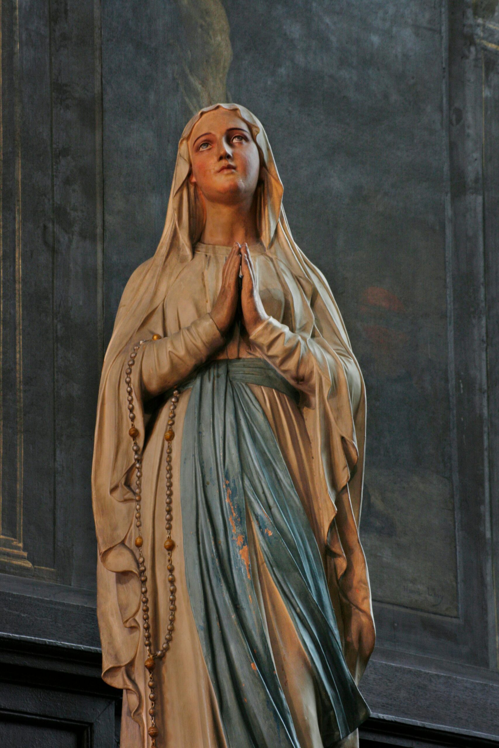 Graceful statue of the Virgin Mary in a praying pose inside a church.